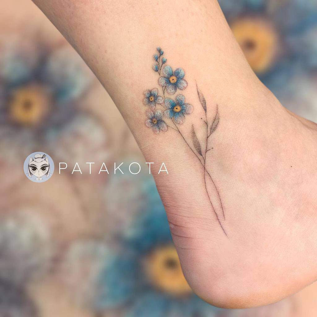 A tattoo of delicate blue forget-me-not flowers with leaves graces a person's ankle