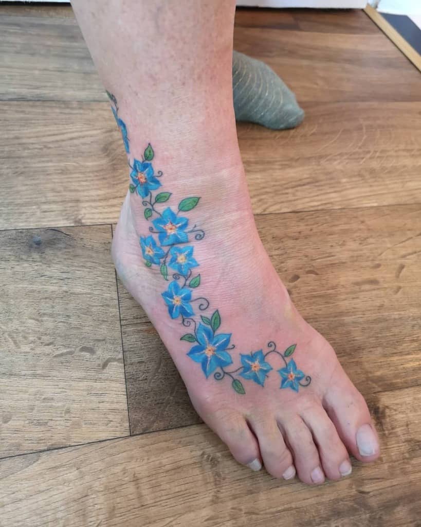 The forget-me-not blue flower tattoo elegantly wraps around an ankle and foot