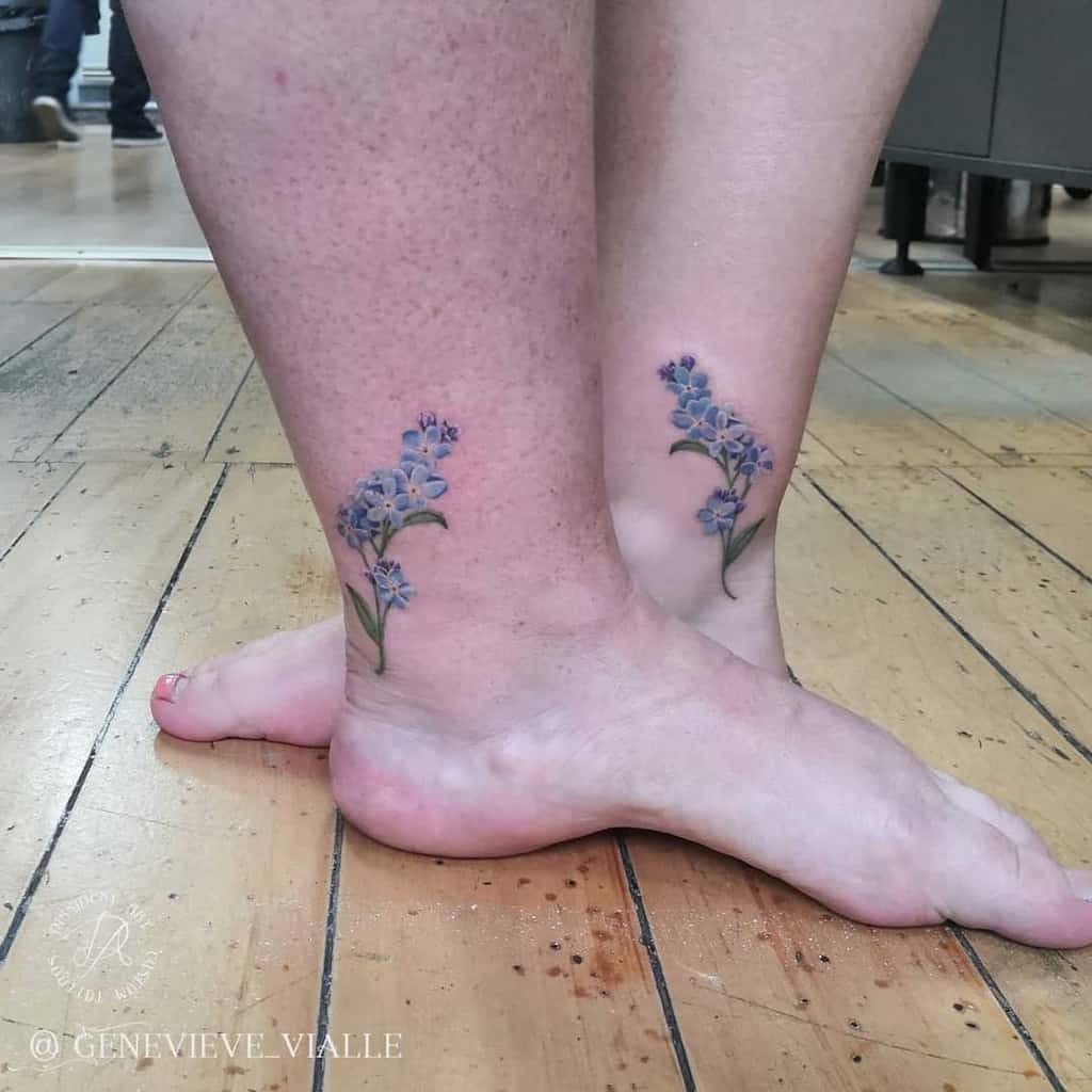 A pair of delicate forget-me-not tattoos on each ankle, featuring soft blue flowers and green stems, inked with subtle shading