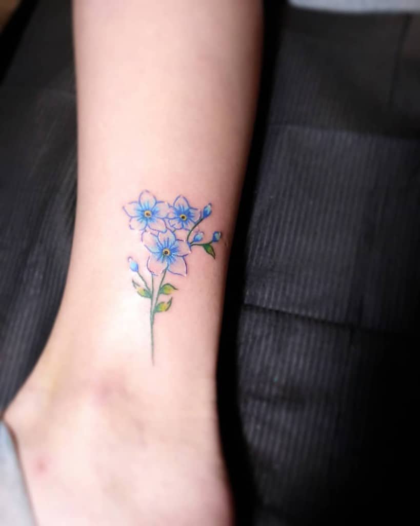 A delicate tattoo of blue forget-me-not flowers on an ankle