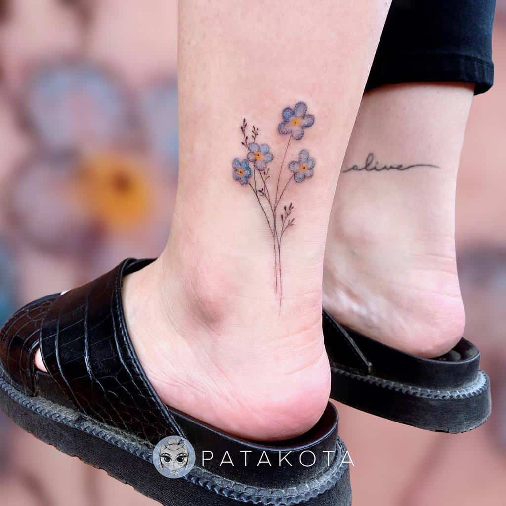 Ankle tattoos of forget-me-not blue flowers and the word "alive"