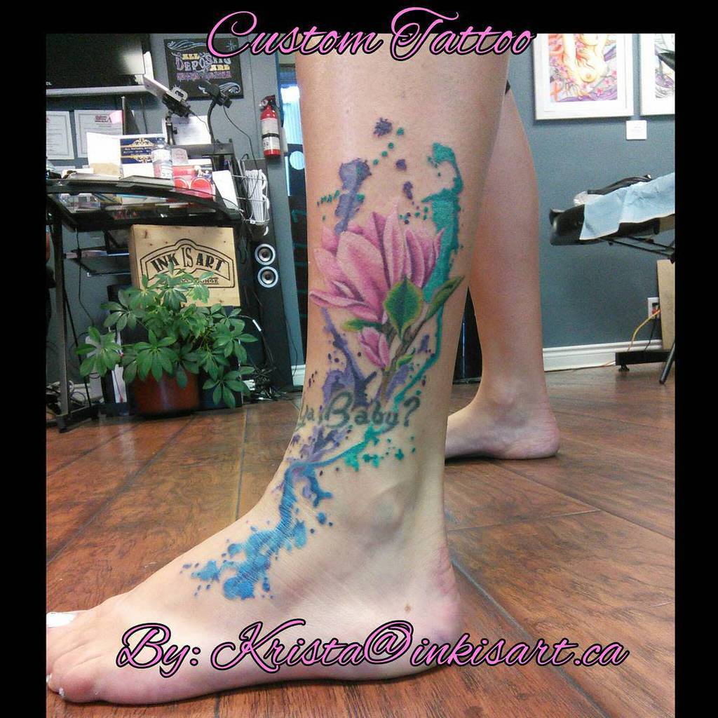 A vibrant floral tattoo adorns the person's foot, featuring magnolia blossoms with stunning blue and purple accents
