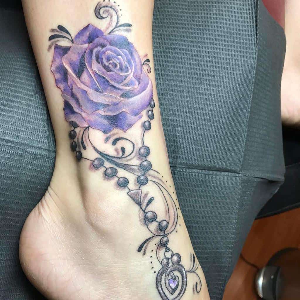 A captivating tattoo of a vibrant purple rose intertwined with decorative black beads elegantly adorns a person's foot and ankle