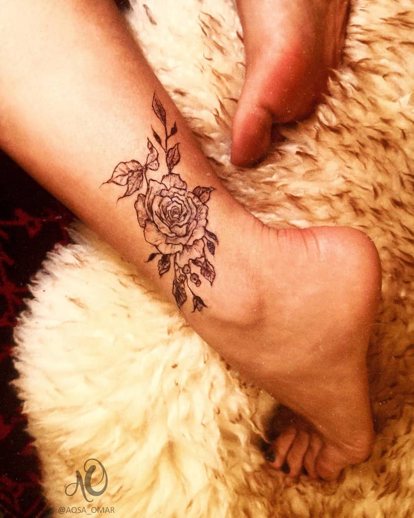 Delicate ankle tattoo featuring a detailed rose with subtle vines and leaves, creating an elegant and minimalist design