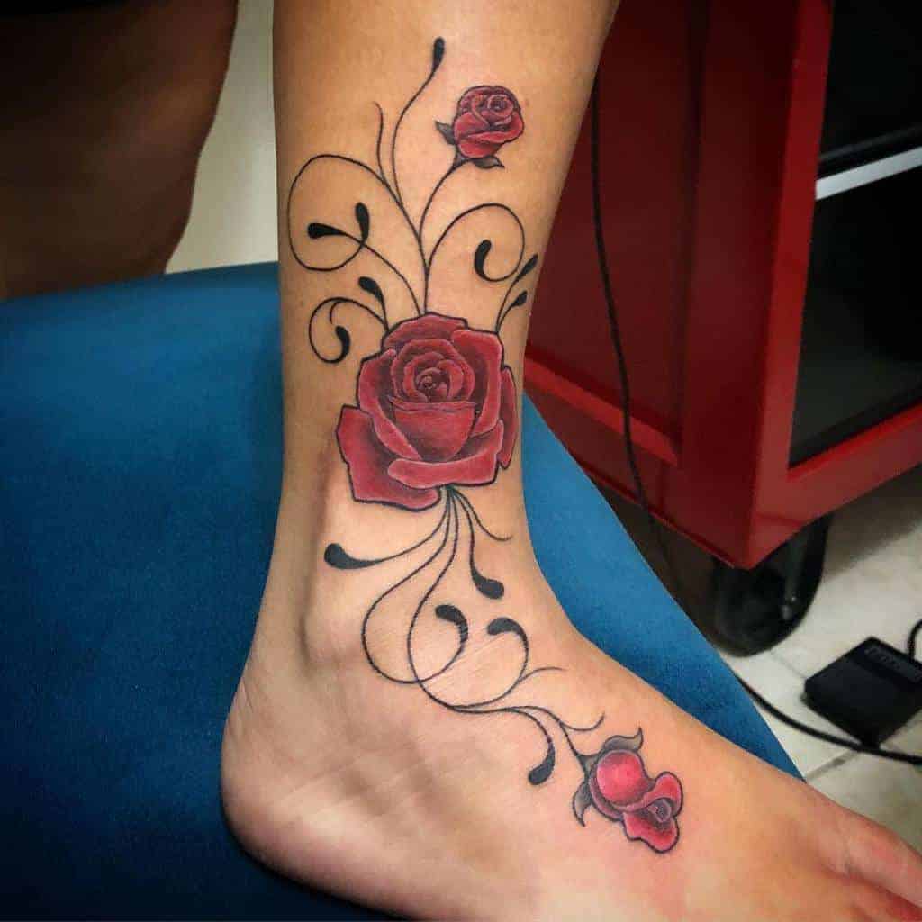 Delicate ankle tattoo featuring a red rose with swirling black vines and smaller rosebud accents