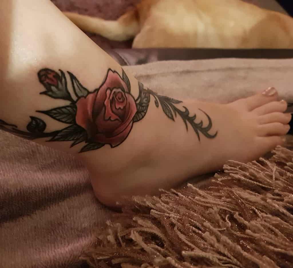 Charming ankle tattoo featuring a deep red rose with green leaves and delicate vines elegantly wrapping around the ankle