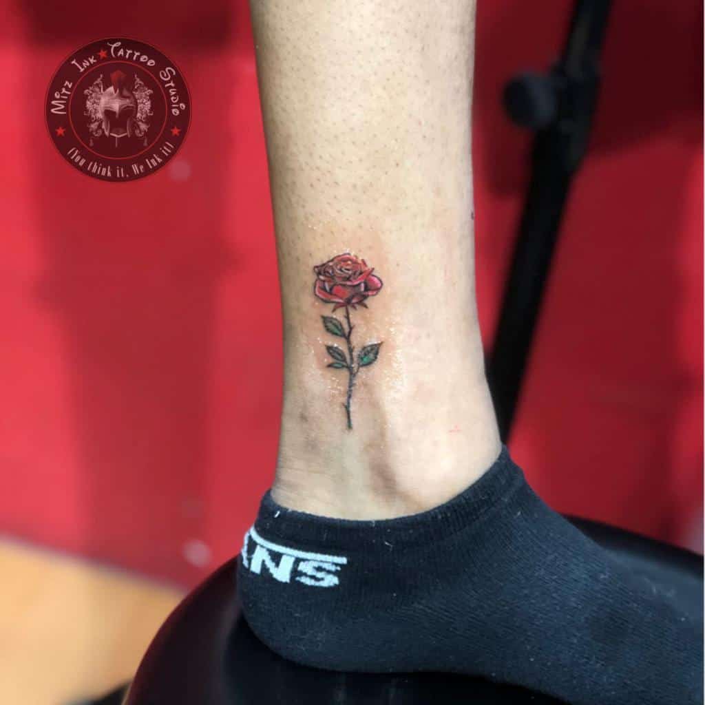 A tattoo of a red rose is on the inside of an ankle