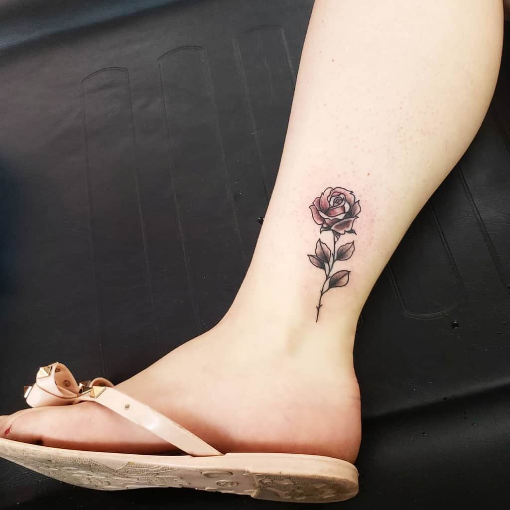 Minimalist rose tattoo on the ankle, featuring delicate shading and fine lines, with a soft pink hue on the petals