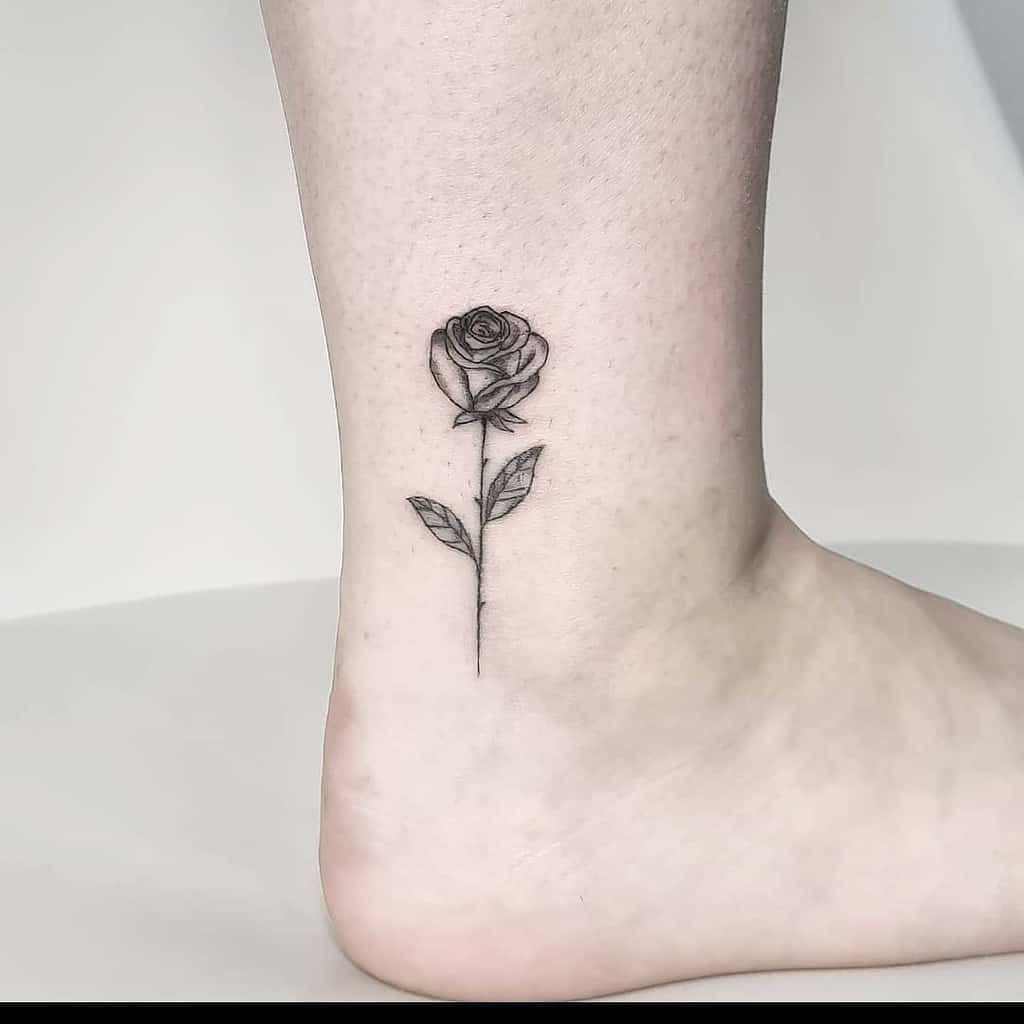 A minimalist black rose tattoo on an ankle
