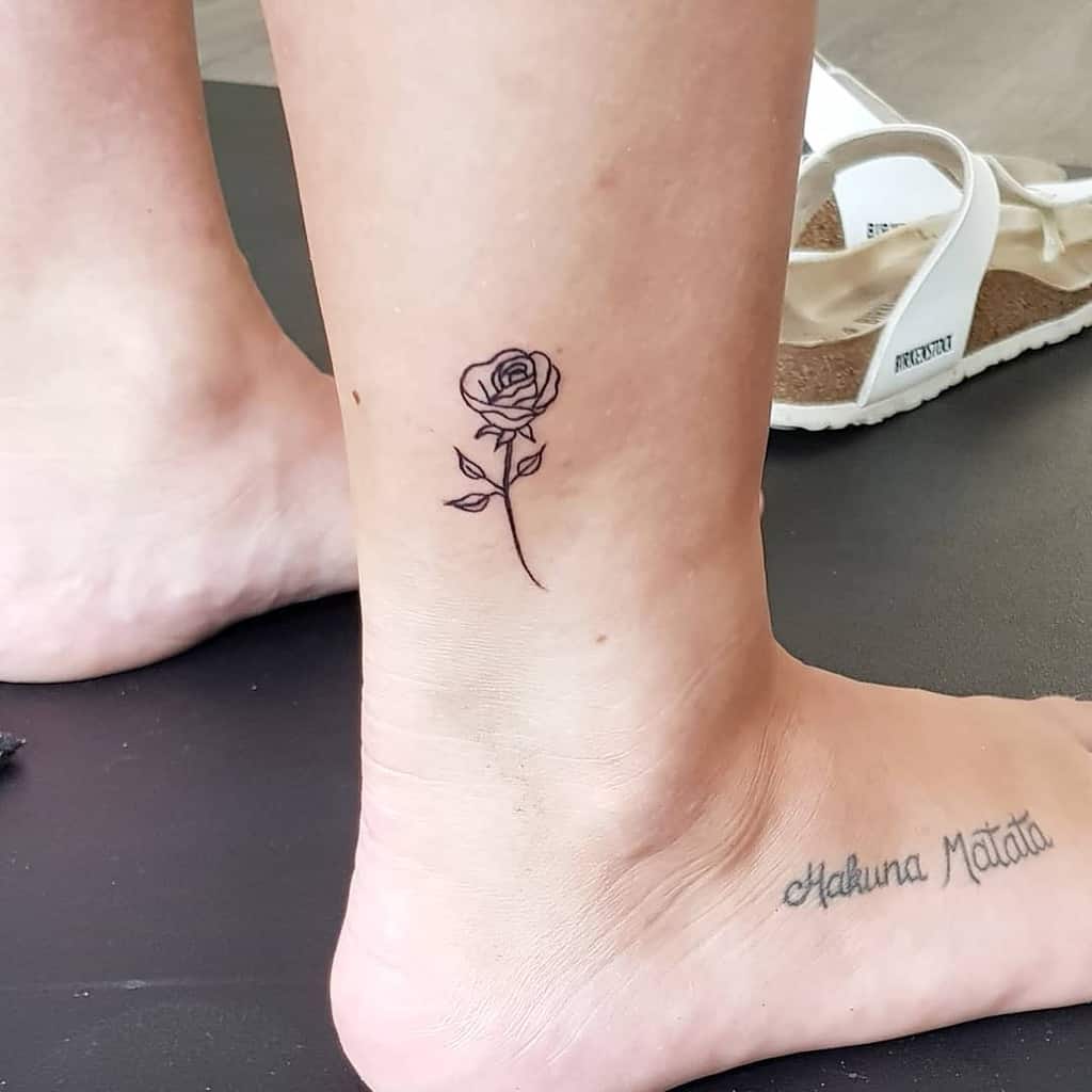 Fine-line rose tattoo on the ankle, featuring a simple black ink design with a delicate stem and leaves