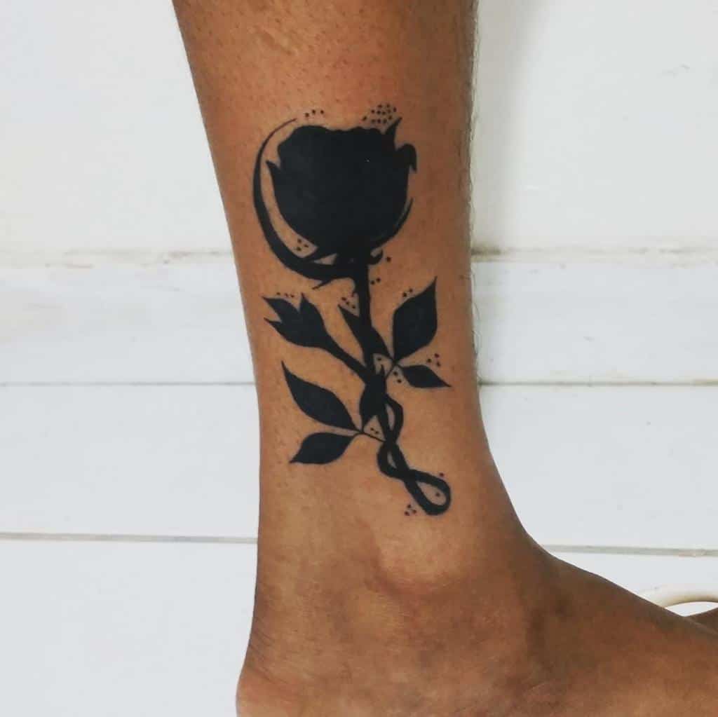 A tribal-infused silhouette tattoo of a rose graces the person's ankle