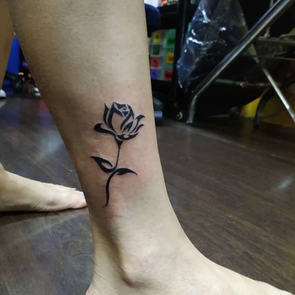 A striking black rose tattoo adorns a person's lower leg, near the ankle, seamlessly incorporating tribal elements into its intricate design