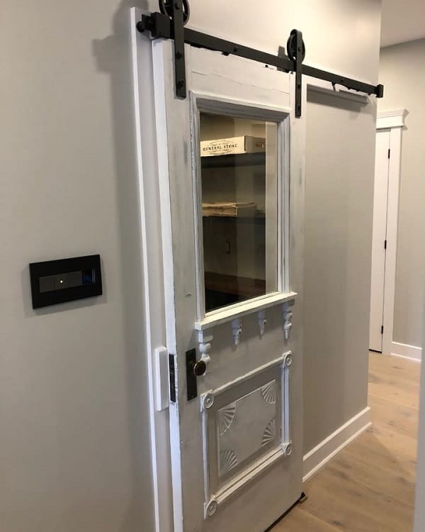Antique sliding barn door with decorative detailing and a glass panel in a modern hallway.