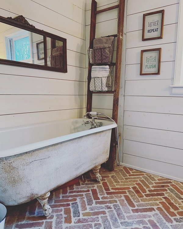 Rustic farmhouse bathroom with a vintage clawfoot tub, wooden ladder for towels, and framed quotes on shiplap walls