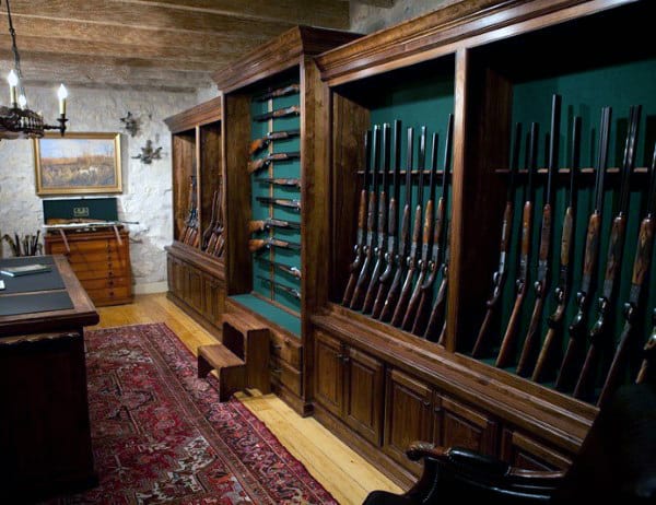 Gun room with dark wood cabinets, green backing, antique rifles, and a decorative rug.