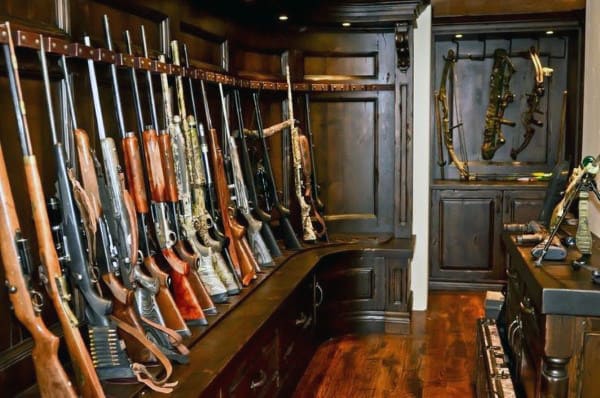 Gun room with dark wooden racks displaying shotguns and a collection of antique weaponry.