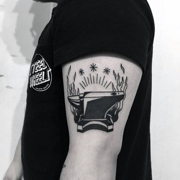 Blackwork anvil tattoo on upper arm with flames, radiant lines, and stars above, giving it a powerful and mystical feel.