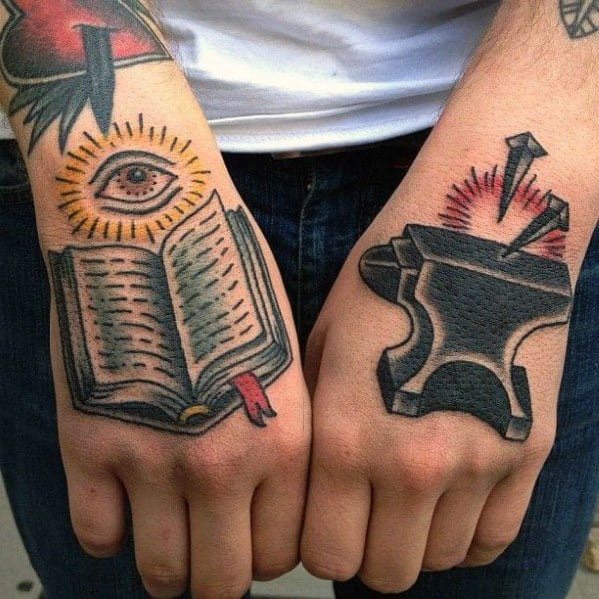 Traditional style hand tattoos featuring an anvil with nails and red sparks on one hand, and an open book with an all-seeing eye on the other.