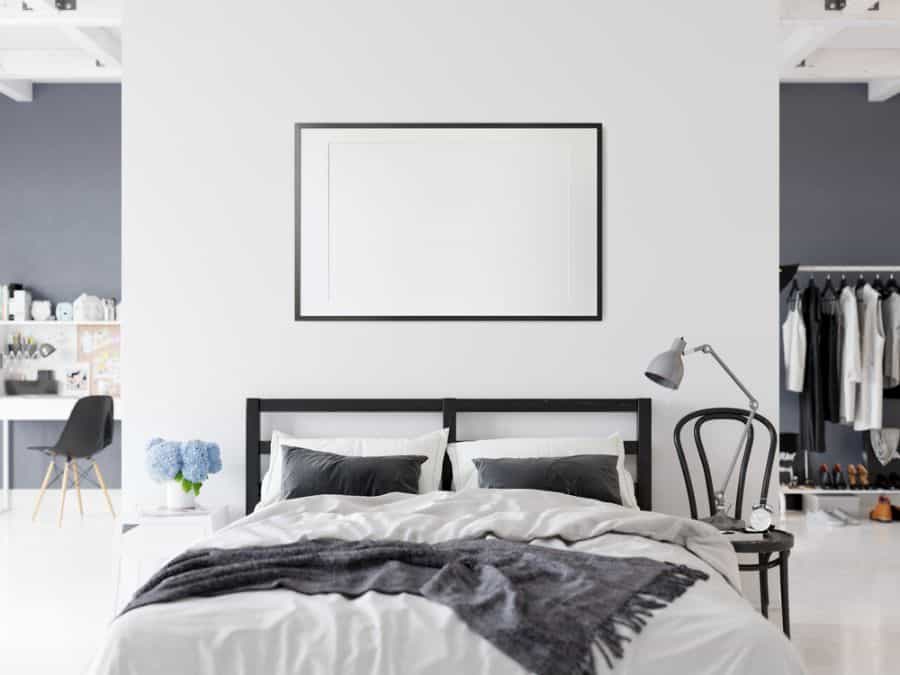 Minimalist bedroom with white walls, black bed frame, grey blanket, and wall art.