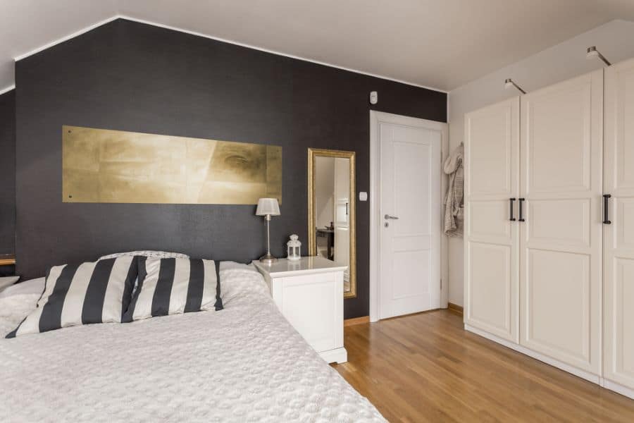 Cozy bedroom with black accent wall, striped pillows, and white wardrobes.