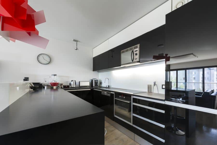 Modern black kitchen with sleek cabinets, white backsplash, and bold red pendant light.
