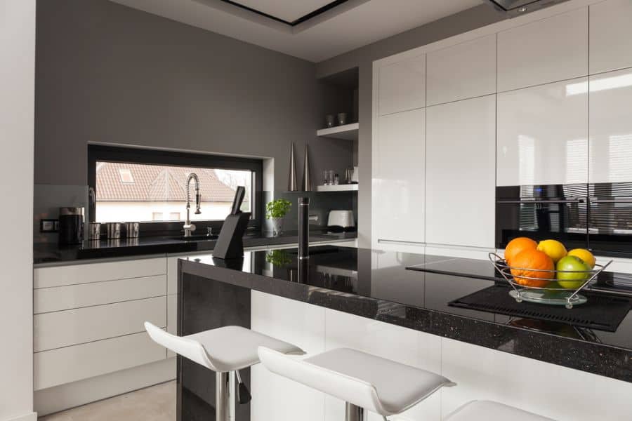 Modern kitchen with white cabinets, black countertops, bar stools, and fruit bowl.