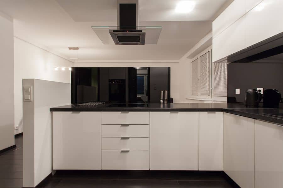 Modern kitchen with white cabinets, black countertops, and stainless steel range hood.