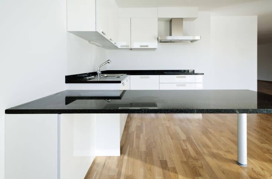Minimalist kitchen with white cabinets, black countertops, and wooden flooring.
