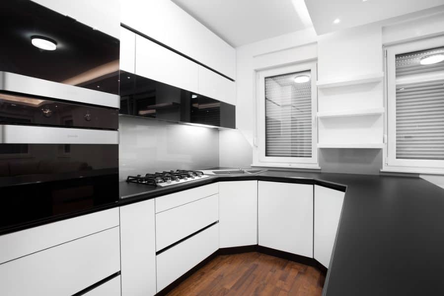 Modern kitchen with white cabinets, black countertops, built-in oven, and open shelves.
