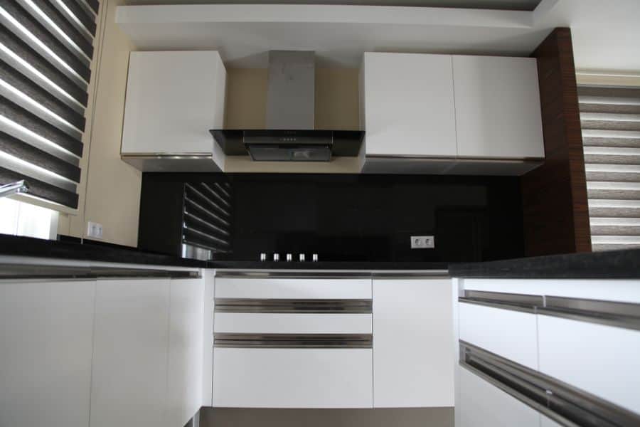 Modern kitchen with white cabinets, black backsplash, and stainless steel range hood.