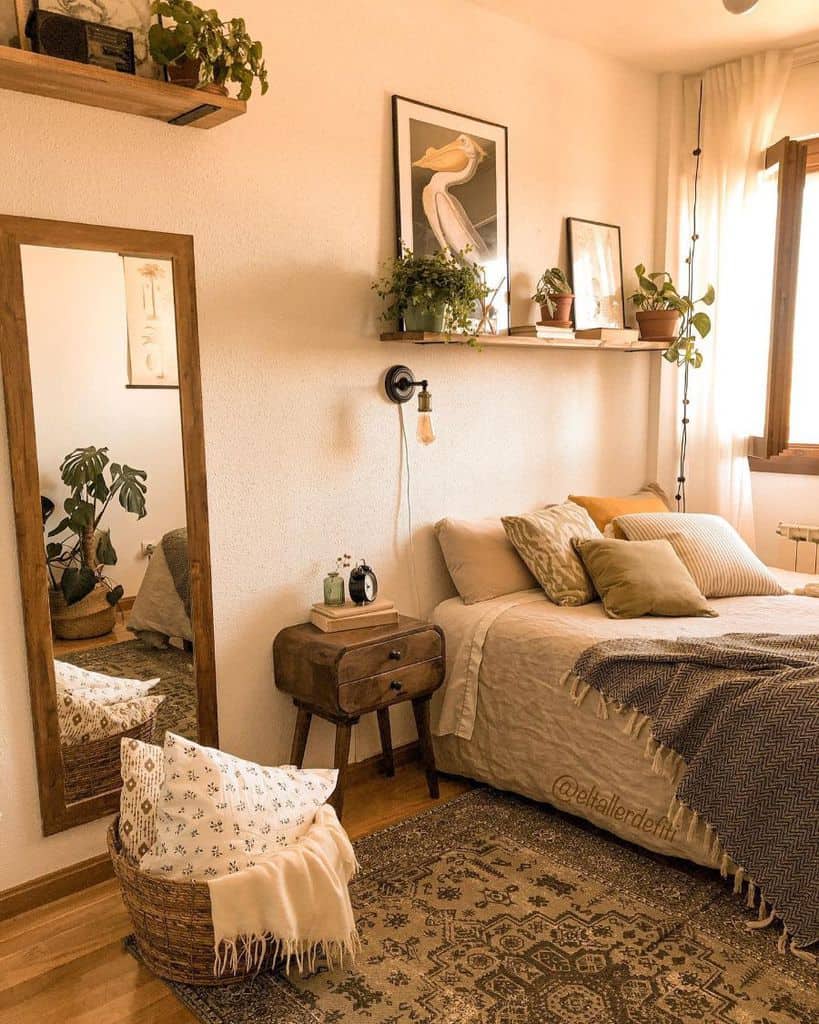 Cozy bedroom with plants, wall art, a wood-framed mirror, and a basket of pillows beside a bed with neutral tones