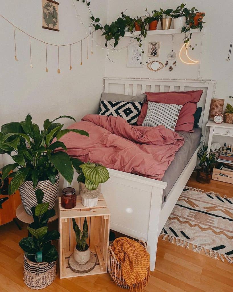 Cozy bedroom with pink bedding, plants, and wall decor, featuring a white bed and wooden accents