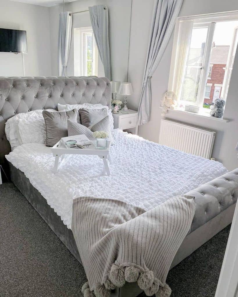 Modern bedroom with tufted grey bed, white bedding, and cozy throw blanket.