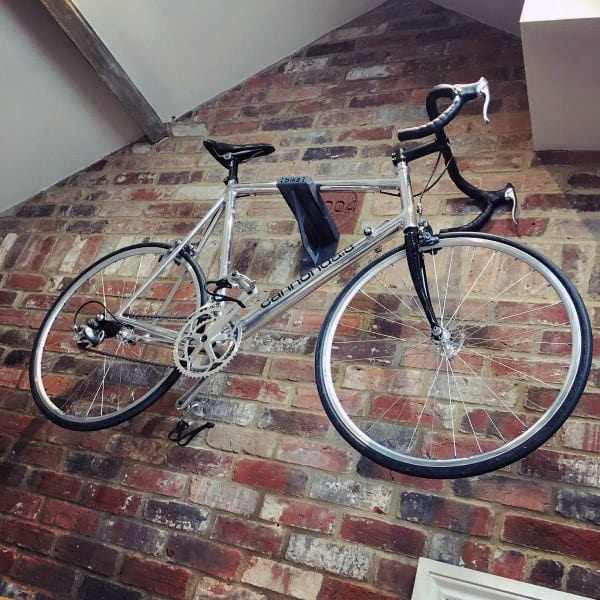 Silver road bike mounted on exposed brick wall for stylish indoor storage.