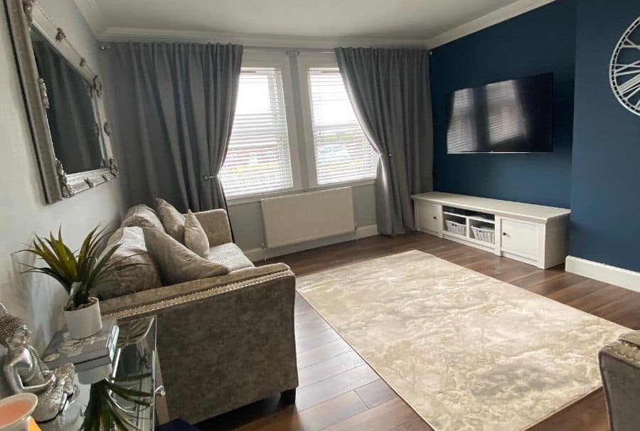 Modern living room with blue accent wall, grey curtains, and beige rug.
