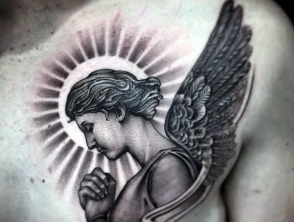 Tattoo of an angel with folded hands, wings, and a radiant halo on a person's chest
