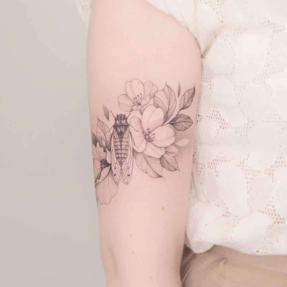 Tattoo of cicada and flowers on an upper arm