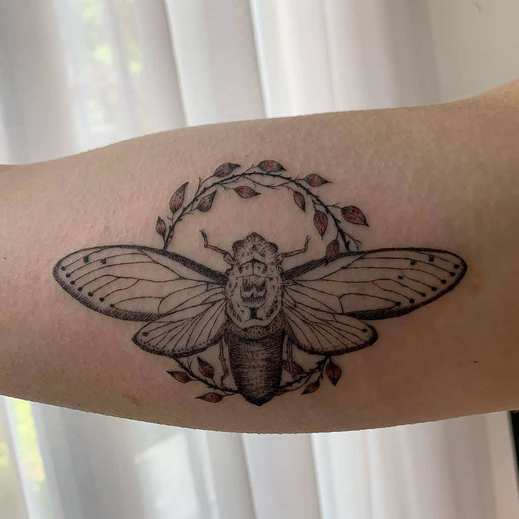Tattoo of a cicada with a circular floral design on an arm