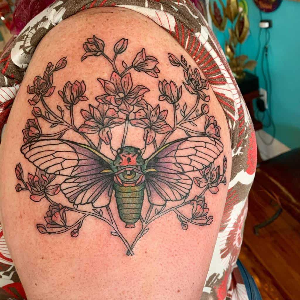 Tattoo of a cicada with wings spread, surrounded by flowering branches on an upper arm