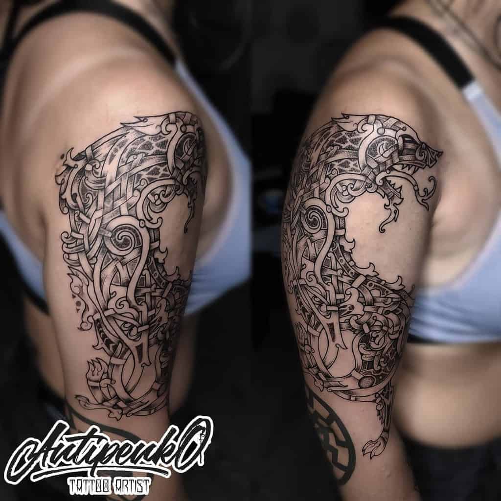 Detailed black ink Norse wolf tattoo featuring intricate knotwork and tribal design on the upper arm