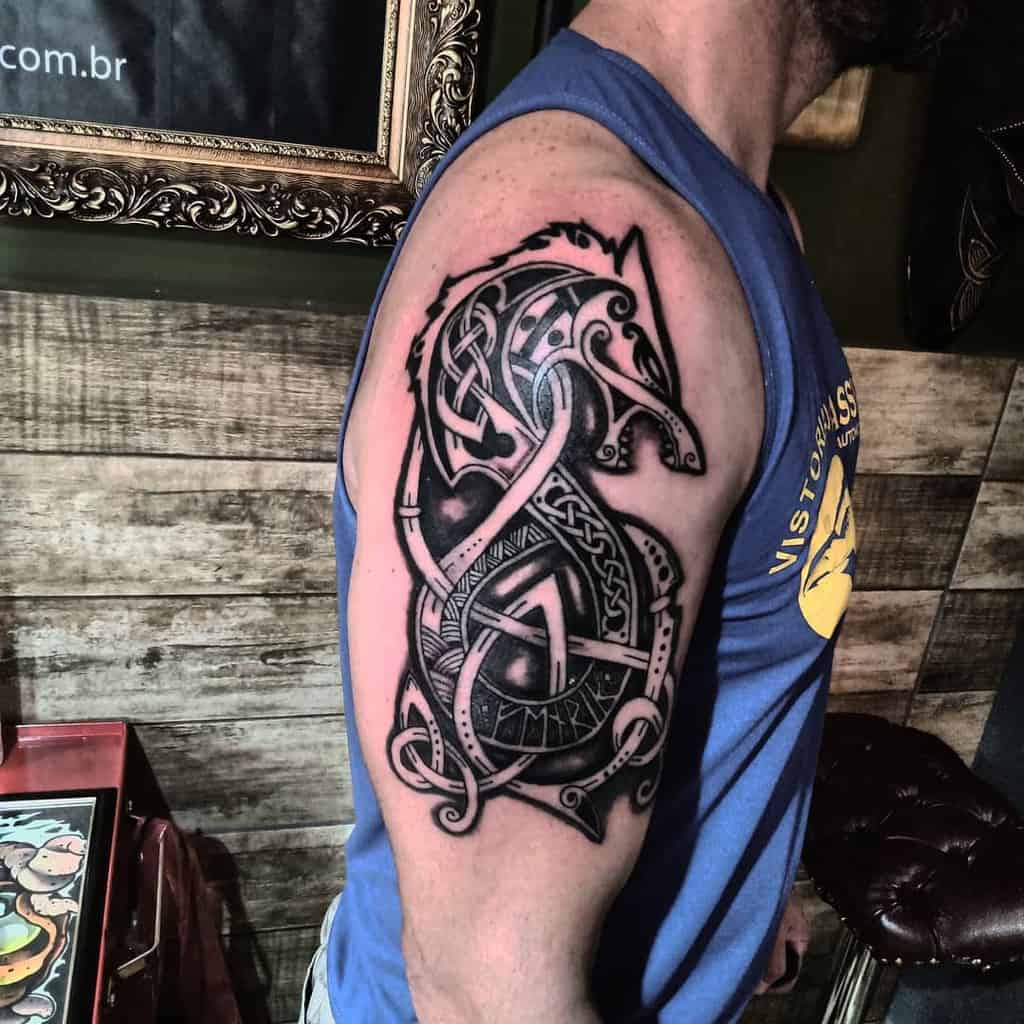 Upper arm tattoo depicting Fenrir in a bold, black-and-grey Norse knotwork design, accentuated with intricate detailing and runic inscriptions