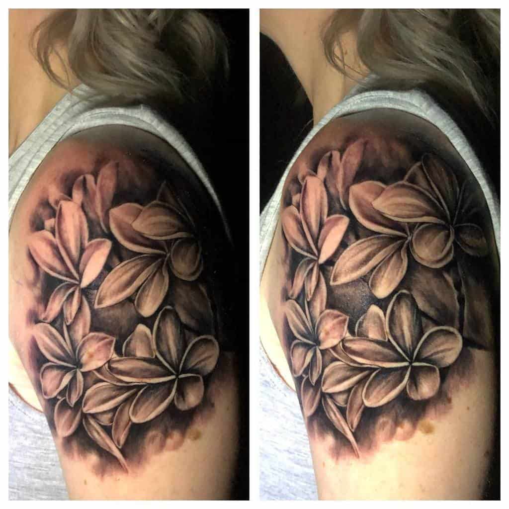 Black and gray Plumeria flower tattoo covering the upper arm, designed with a soft gradient background to enhance depth and floral detail