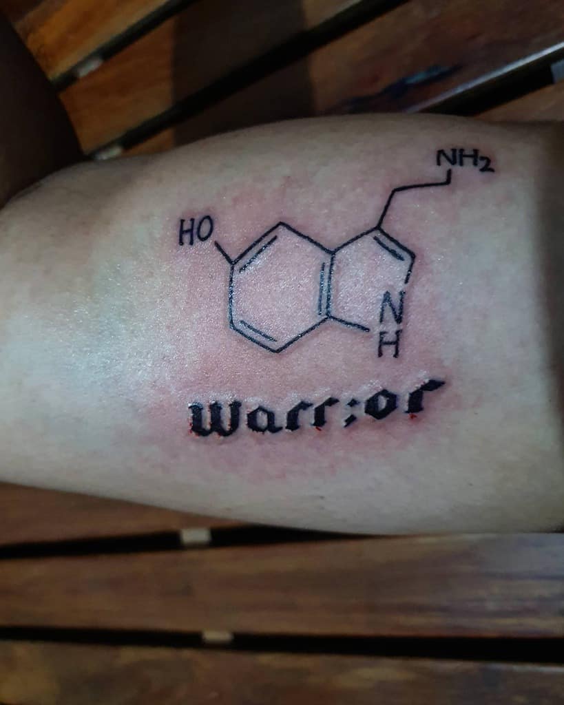 Tattoo of the serotonin molecule elegantly inked above the word "Warrior" graces an arm