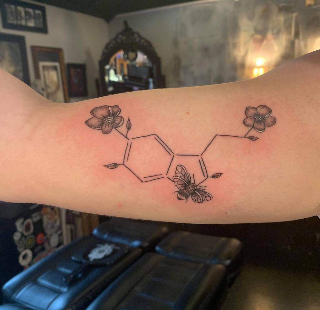 An arm tattoo elegantly weaves the chemical structure of serotonin with delicate flowers, creating a unique blend of science and nature