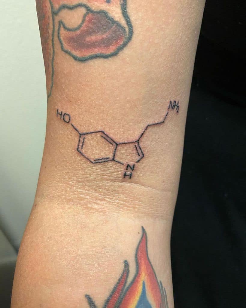 A tattoo of the serotonin molecular structure adorns a forearm, seamlessly surrounded by vibrant, colorful designs