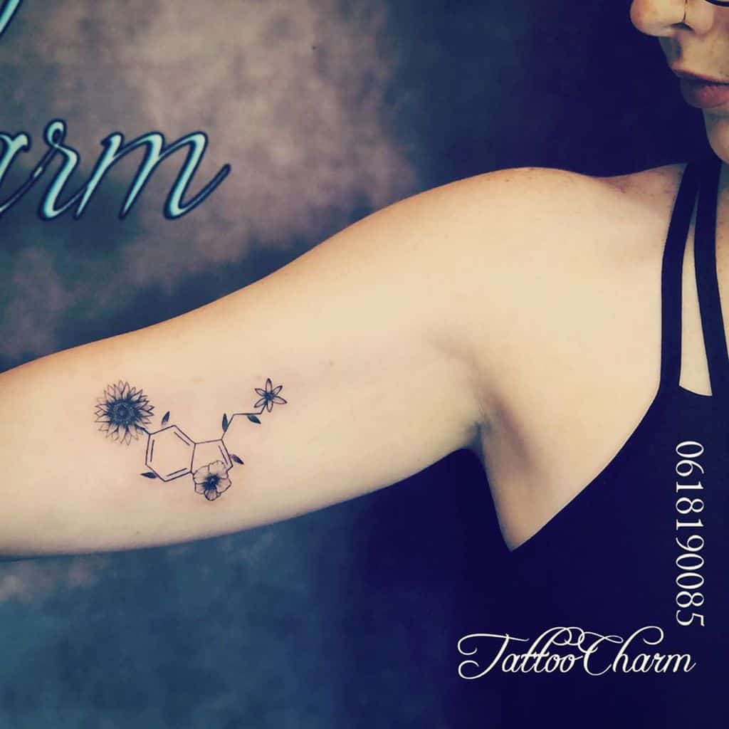 Tattoo of a serotonin chemical structure intertwined with delicate flowers on an upper arm