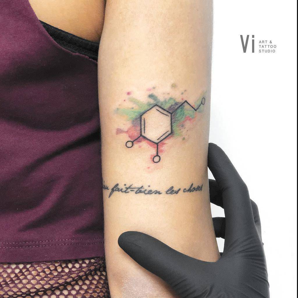 Tattoo on an arm featuring the hexagonal chemical structure of serotonin with elegant French text beneath