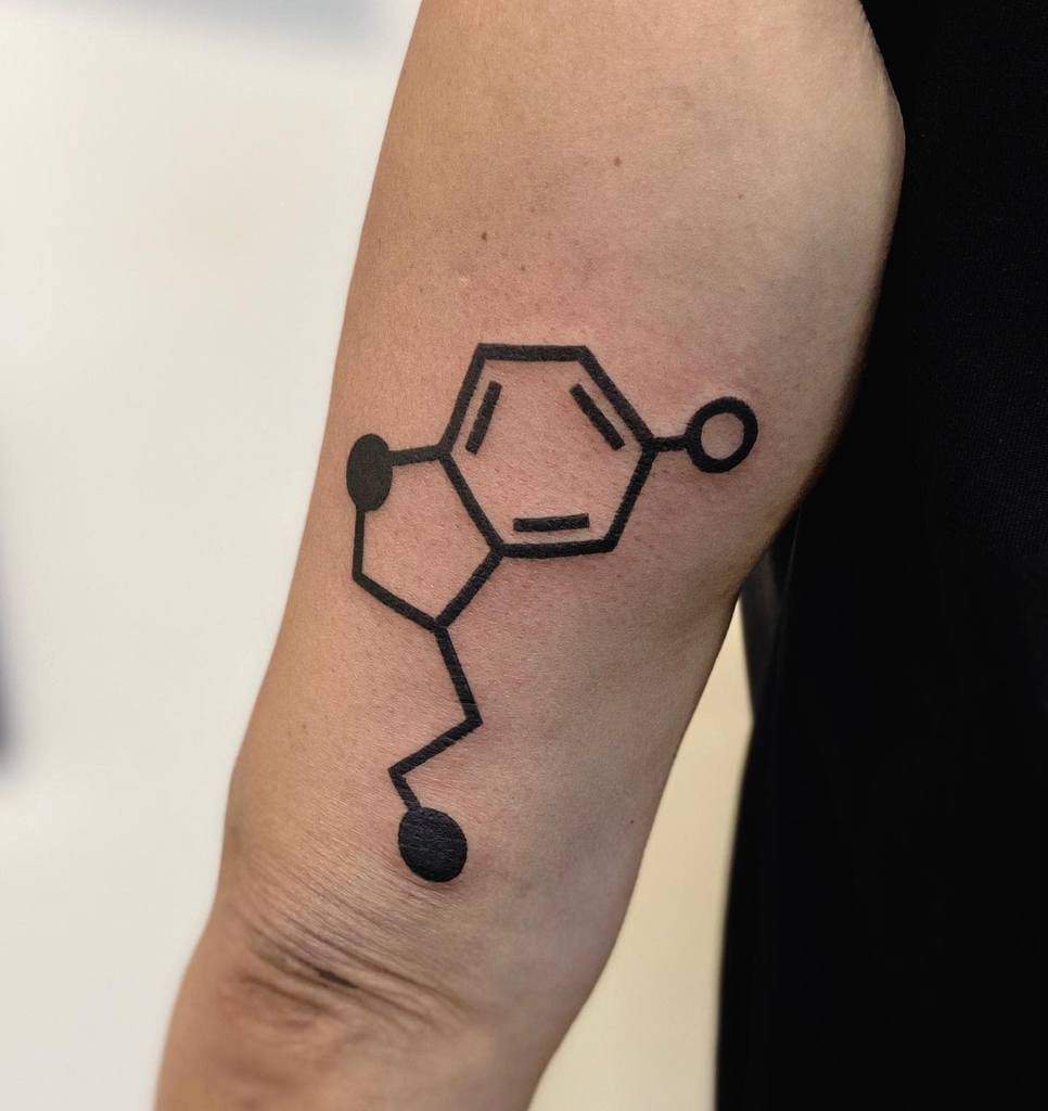 A tattoo of the serotonin chemical structure graces a person's arm, featuring intricate hexagons and lines