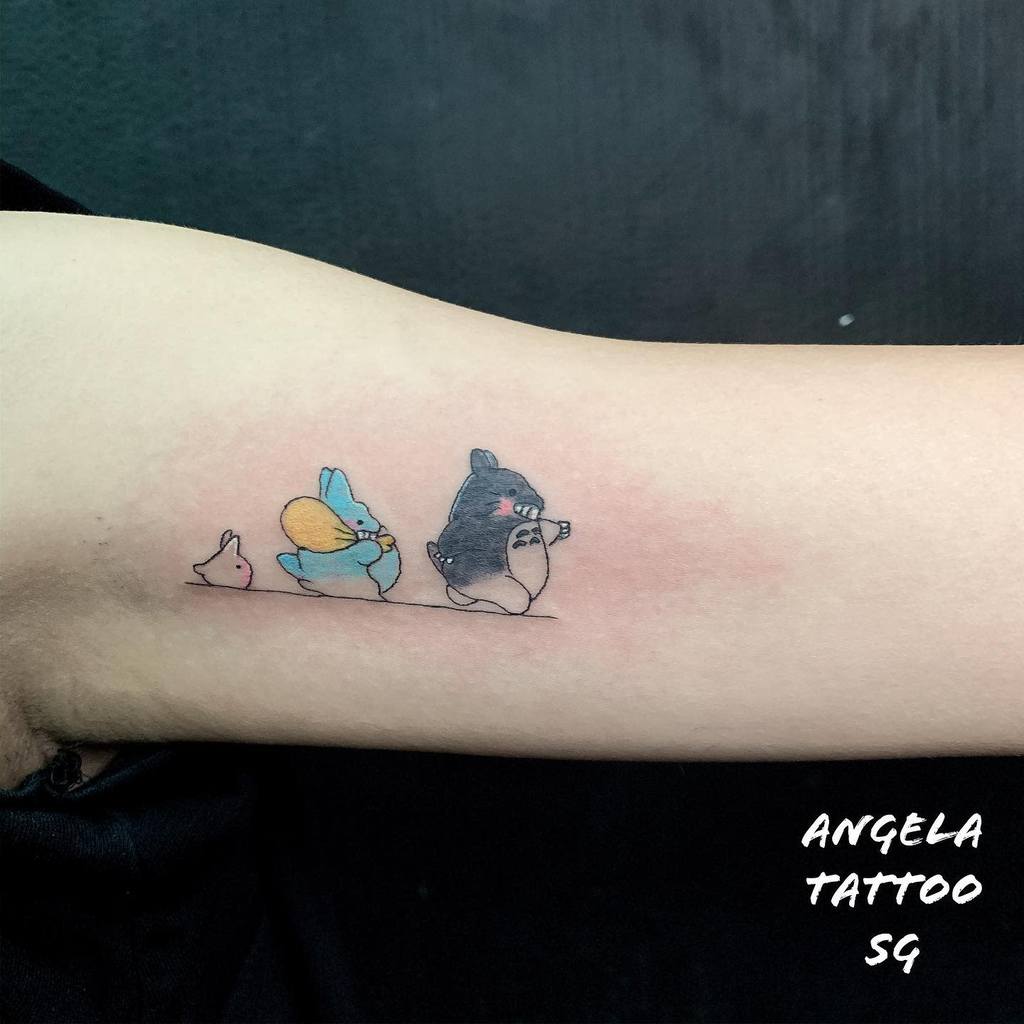 Colorful Totoro tattoo on the inner arm, featuring Totoro and his small companions in a cute, playful line-up