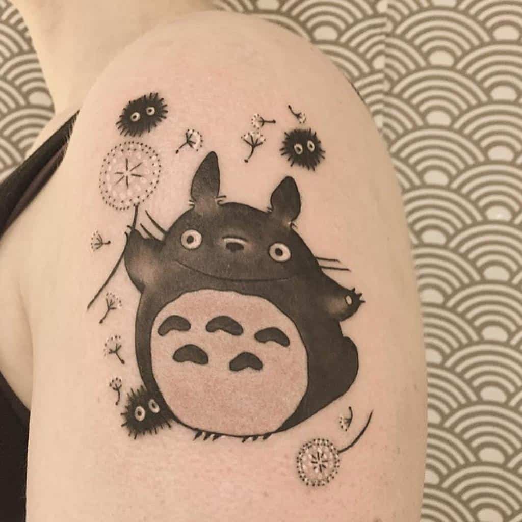 A charming shoulder tattoo featuring Totoro surrounded by floating dandelion seeds and playful soot sprites